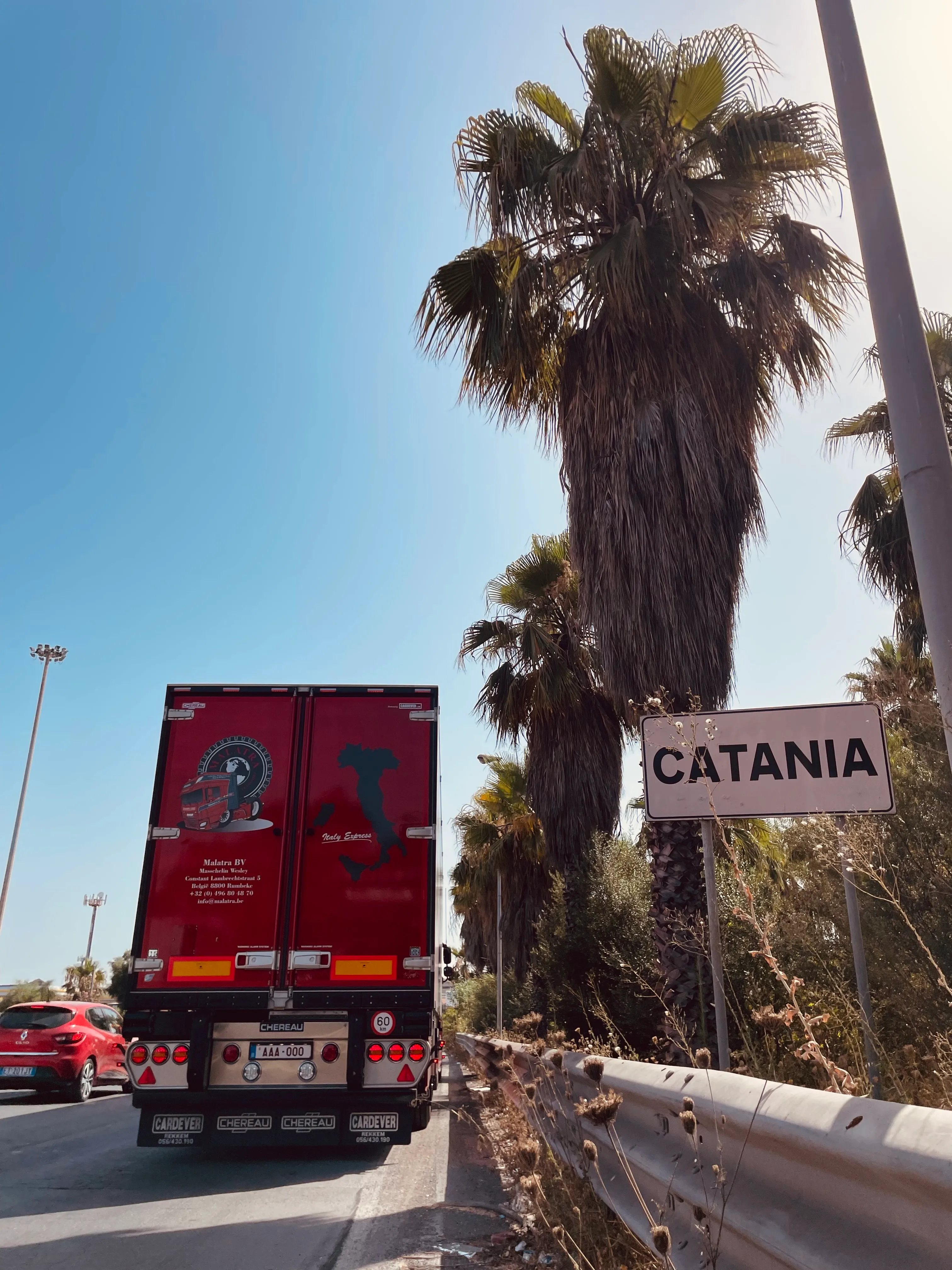 Achterzijde van een Malatra-trailer met een wegwijzer richting Catania op de achtergrond