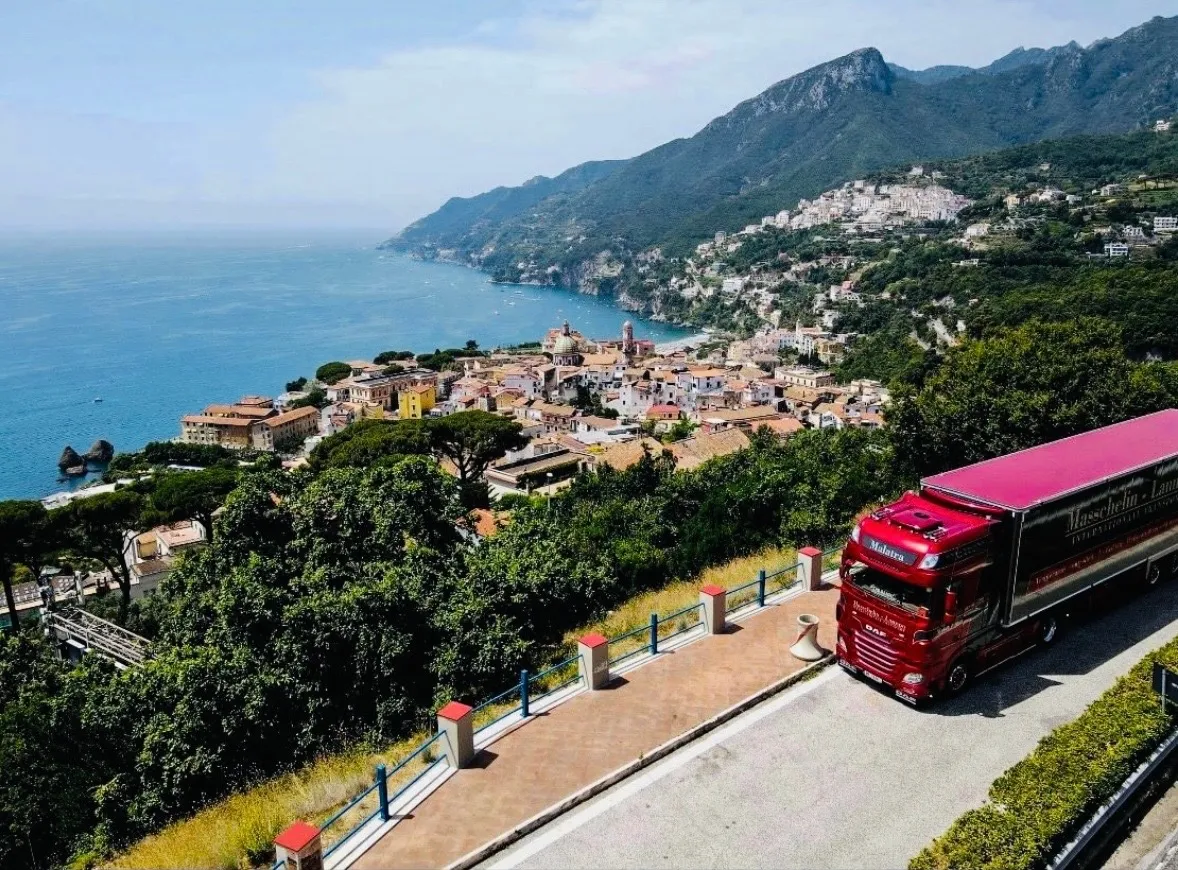Luchtfoto van een Malatra-trekker die over de kustweg van Amalfi rijdt, met uitzicht op zee en de kustdorpjes